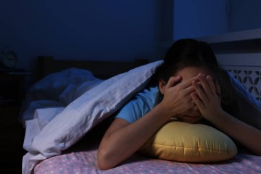 Gece yatakta yorganın altında yastıkla korkan kız.