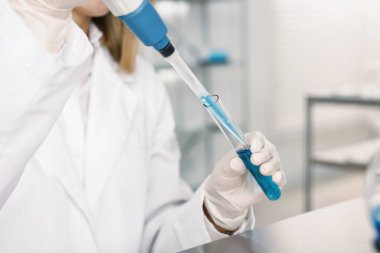 Mikro pipetli ve test tüplü bilim adamı laboratuarda çalışıyor, yakın plan.