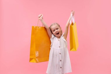 Pembe arka planda alışveriş torbaları olan küçük kız.
