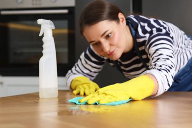 Kadın temizlik malzemesi kullanırken ahşap masayı kapalı alanda bez parçasıyla siliyor, seçici odaklanma