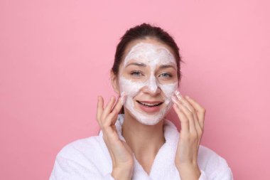 Spa günü. Güzel bir kadın pembe arka planda yüzüne maske takıyor.
