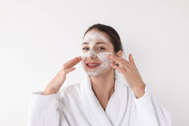 Spa günü. Güzel bir kadın beyaz arka planda yüzüne maske takıyor.