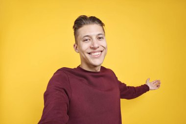 Mutlu adam selfie çekiyor ve turuncu arka plandaki arkadaşları ya da konukları selamlıyor.