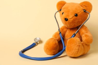 Pediatri konsepti. Bej arka planda steteskoplu oyuncak ayı, metin için boşluk