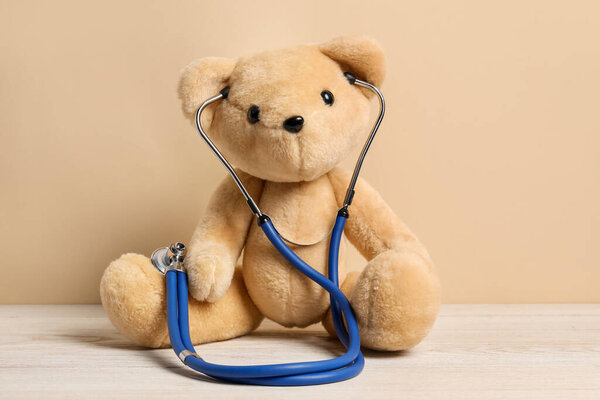 Pediatrics concept. Teddy bear with stethoscope on wooden table against beige background