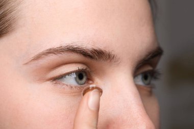 Genç bir kadın bulanık arka plana renkli lens takıyor, yakın plan.