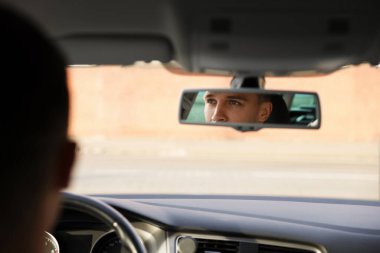 Modern arabanın direksiyonundaki sürücü, dikiz aynasından bakıyor.