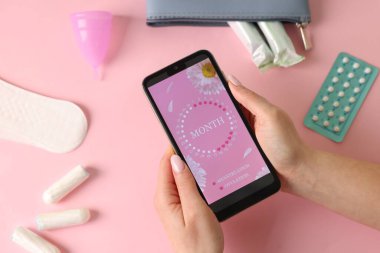 Regl. Pembe arka planda periyot takvim uygulaması olan akıllı telefonu tutan kadın, üst görünüm