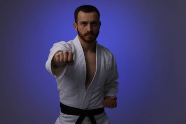 Üniformalı bir adam koyu mor arka planda karate yapıyor.