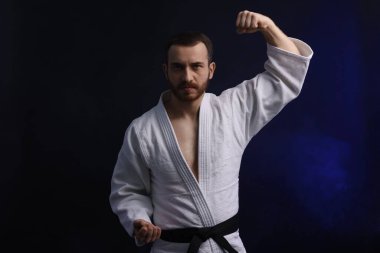 Üniformalı bir adam karanlık arka planda karate yapıyor.
