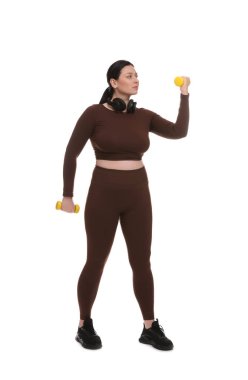 Ayrıca spor elbiseli bir kadın beyaz arka planda dambıllarla egzersiz yapıyor.