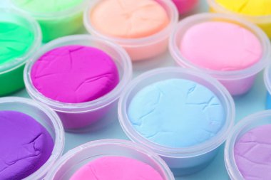 Açık mavi arka planda plastik kavanozlardaki farklı renkli modelleme killeri, yakın plan