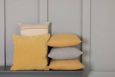 Gri duvarın yanındaki çekmecelerin üzerindeki yumuşak dekoratif yastıklar.