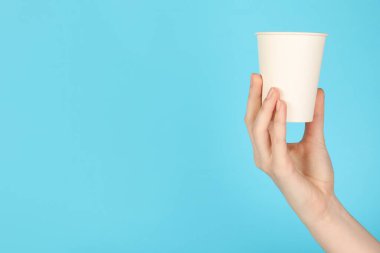 Açık mavi arka planda kağıt bardak tutan kadın, yakın plan. Tasarım için model