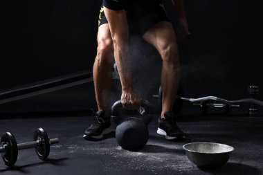 Siyah arka planda bir kase talk pudrasının yanında kettlebell ile antrenman yapan adam, yakın plan.