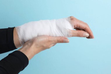 Bileğinde bandaj olan kadın açık mavi arka planda, yakın plan.