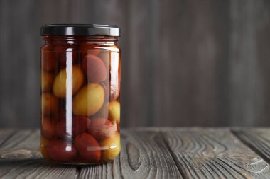 Cam kavanozdaki turşulu zeytinler ahşap masa üzerinde gri arkaplan, metin için boşluk