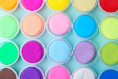 Açık mavi arka planda plastik kavanozlarda farklı renklerde kil modelleme.