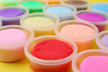 Sarı arka planda plastik kavanozlardaki farklı renkli modelleme killeri, yakın plan.