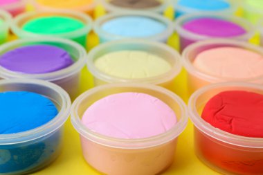 Sarı arka planda plastik kavanozlardaki farklı renkli modelleme killeri, yakın plan.