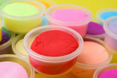 Sarı arka planda plastik kavanozlardaki farklı renkli modelleme killeri, yakın plan.