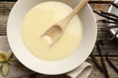 Yoğunlaştırılmış süt, kaşık, vanilya kapsülleri ve çiçek ahşap masada, düz yatıyordu.