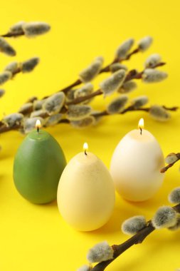 Beautiful burning egg shaped candles and pussy willow on yellow background, closeup. Easter decor
