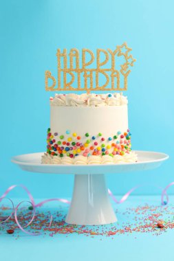 Renkli süslemeli nefis bento keki, açık mavi masa üzerinde süslemeli ve serpentin şeritli.