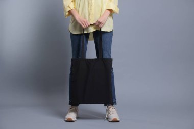 Gri arka planda boş alışveriş çantası olan bir kadın, yakın plan. Tasarım için model