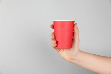 Gri arka planda kağıt bardak tutan kadın, yakın plan. Tasarım için model