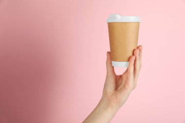 Pembe arka planda kağıt bardak tutan kadın, yakın plan. Tasarım için model