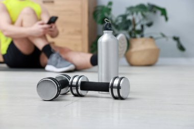 Kapalı mekanda akıllı telefonu olan adam, dambıl ve termosu olan adama odaklan.