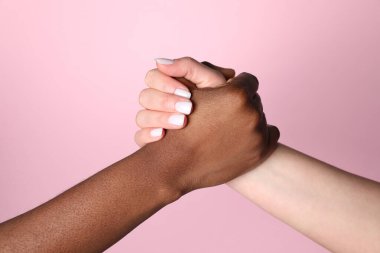 Irkçılığı bırak. Açık pembe arka planda el ele tutuşan farklı ten renginde insanlar, yakın plan