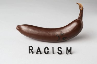 Kelime ırkçılığı ve koyu renkli muz açık gri arka planda üzgün yüz.