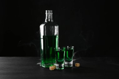 Absinthe shot bardakları, şişe ve esmer şeker siyah arka planda dumanlı
