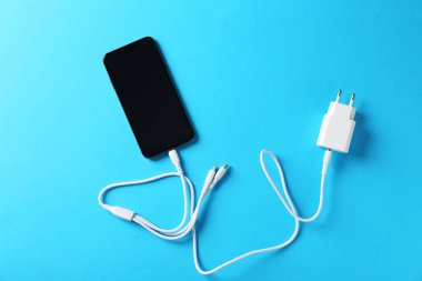 Açık mavi arka planda akıllı telefona bağlı üç şarj kablosu, üst görünüm