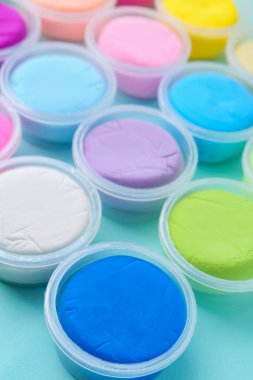 Açık mavi arka planda plastik kavanozlardaki farklı renkli modelleme killeri, yakın plan
