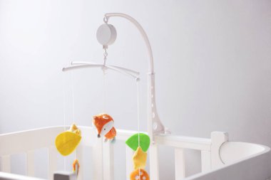 Çocuk odasındaki açık gri duvarın yanında şirin bebek arabası olan bir beşik.