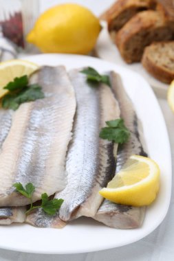 Marinated herring fillets with lemon and parsley on white table, closeup