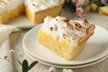 Kahverengi kremalı bir dilim turta ve açık renkli bir masa üzerinde çiçekler, yakın plan.