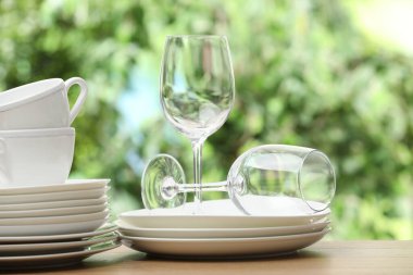 Farklı temiz bulaşık takımları, kupalar ve bardaklar ahşap masada bulanık yeşil arka plana karşı.