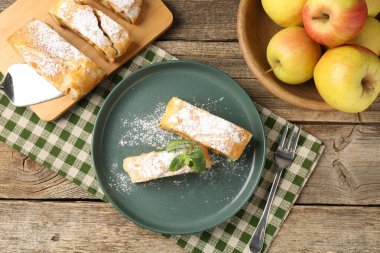 Lezzetli elmalı turta parçaları pudra şekeri, nane, meyve ve çatal ile ahşap masa, düz yatıyordu.