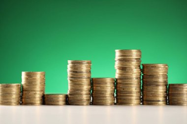 Yeşil arkaplana karşı beyaz masadaki bozuk para yığınları, yakın plan