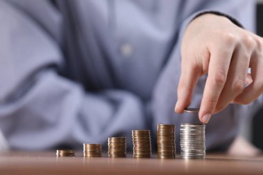 Adam ahşap masadaki para yığınlarına para koyuyor, yakın plan.