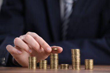 Adam ahşap masadaki para yığınlarına para koyuyor, yakın plan.
