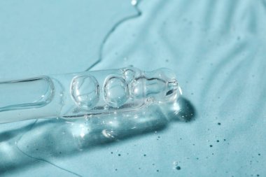 Açık mavi arkaplanda kozmetik serumlu boru, yakın plan.