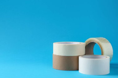 Açık mavi arkaplanda farklı yapıştırıcı bantların ruloları, metin için boşluk