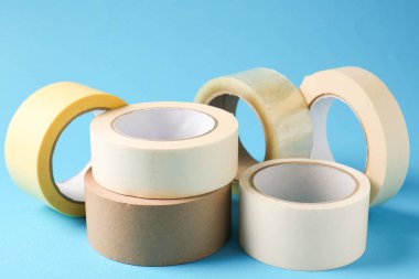 Açık mavi arkaplanda farklı yapışkan bantların ruloları, yakın plan