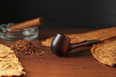 Tütün, kuru yapraklar, puro ve sigara piposu ahşap masada, yakın plan.