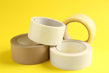 Sarı arka planda farklı yapışkan bantların ruloları, yakın plan.